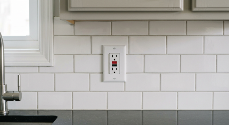 White GFCI outlet on a kitchen backsplash above a countertop for safe troubleshooting when it keeps tripping.