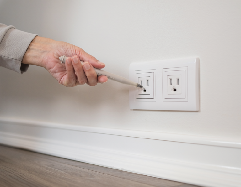 Homeowner safely holding a non-contact voltage tester near the face of an intact wall outlet without touching the outlet or inserting the tester.