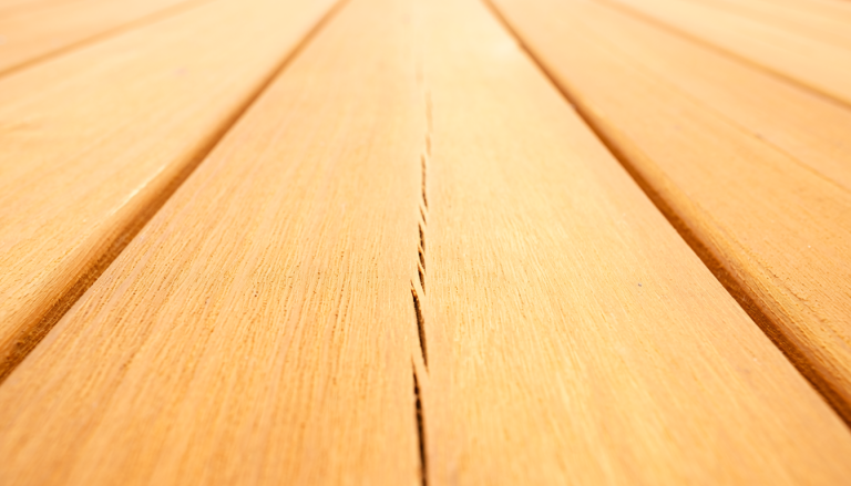 Close-up of a natural wood deck board with a narrow lengthwise crack running along the grain.