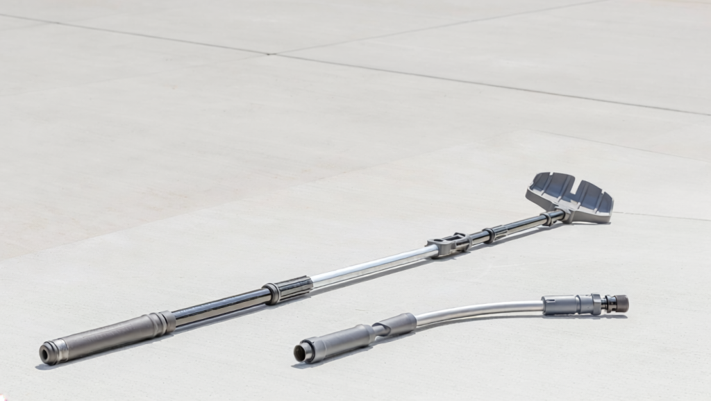 Telescoping gutter-cleaning pole with a scoop or claw head and a curved hose wand lying on a clean driveway.