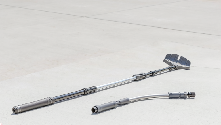 Telescoping gutter-cleaning pole with a scoop or claw head and a curved hose wand lying on a clean driveway.