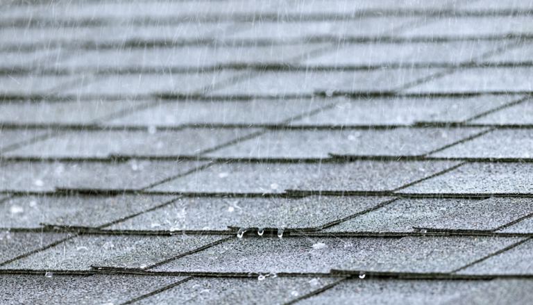 Residential asphalt-shingle roof in heavy rain with a small localized leak area.