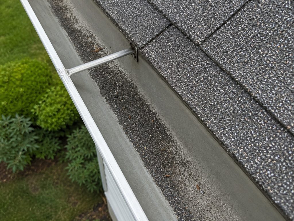 Asphalt-shingle granules collected in a residential gutter below the roof edge.