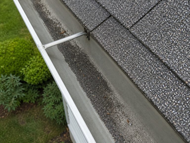 Asphalt-shingle granules collected in a residential gutter below the roof edge.