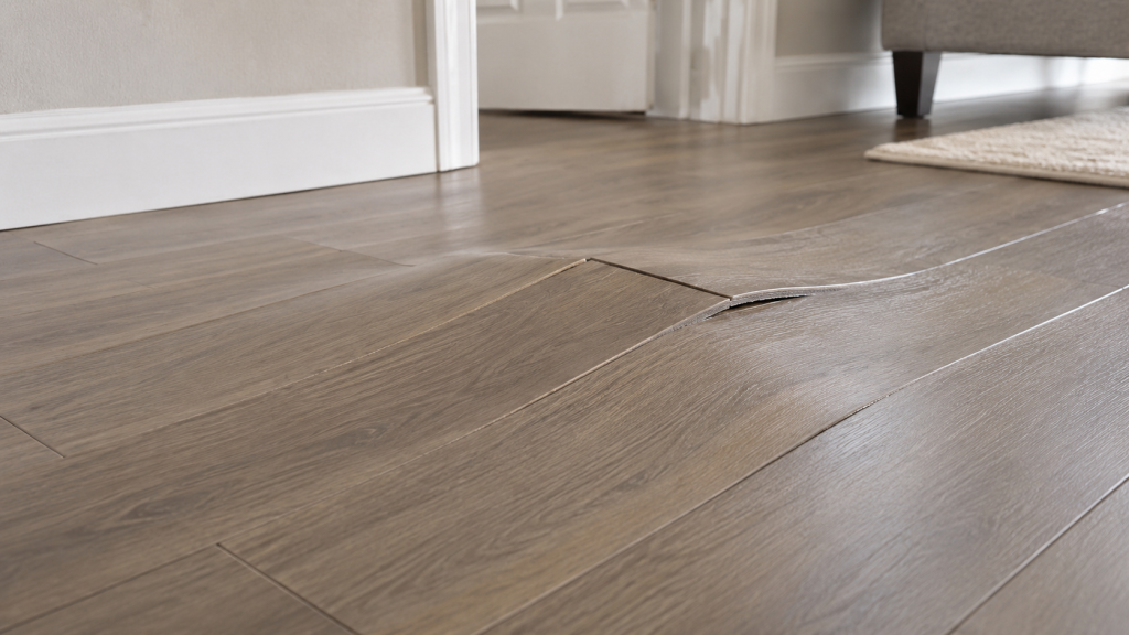 Buckled vinyl plank flooring with raised and tented planks in a residential room.
