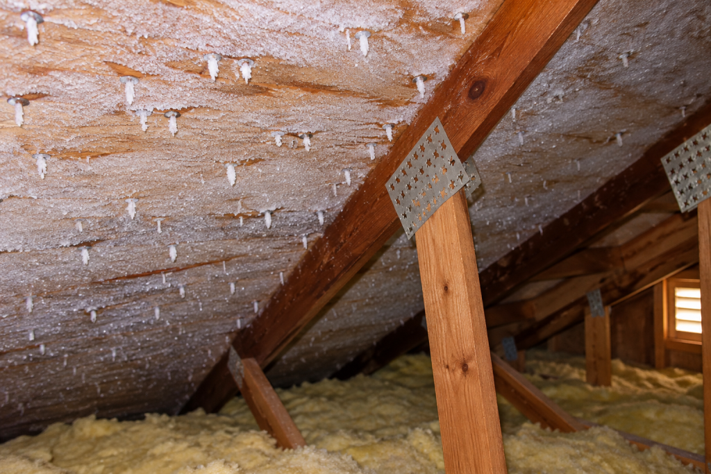 Frost buildup on attic roof sheathing and metal fasteners above insulated attic framing during cold weather.